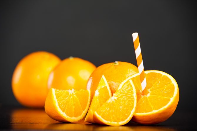 Fresh Oranges with a drinking straw on slate plate