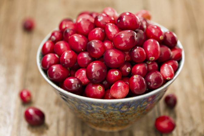 "A high angle close up shot of a colorful ceramic bowl full of raw, fresh red cranberries."